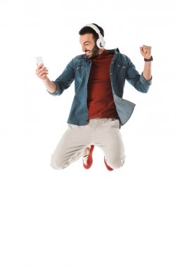 akıllı telefon kullanırken kulaklık heyecanlı adam atlama ve evet jest beyaz izole gösteren
