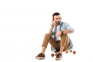uzun tahta üzerinde oturan ve beyaz izole akıllı telefon üzerinde konuşan gülümseyen adam