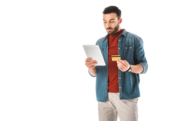 thoughtful man holding credit card while using digital tablet isolated on white