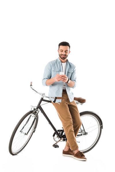 handsome bearded man with bicycle smiling while using smartphone isolated on white