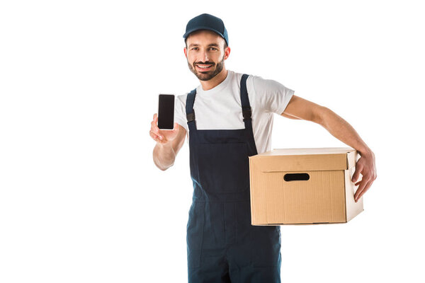 cheerful delivery man with cardboard box holding smartphone with blank screen and looking at camera isolated on white