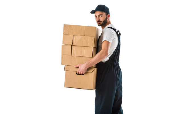 serious delivery man carrying cardboard boxes and looking at camera isolated on white