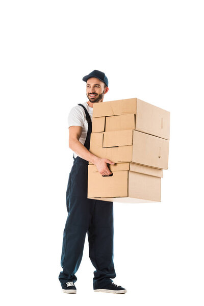 smiling delivery man carrying cardboard boxes and looking away isolated on white