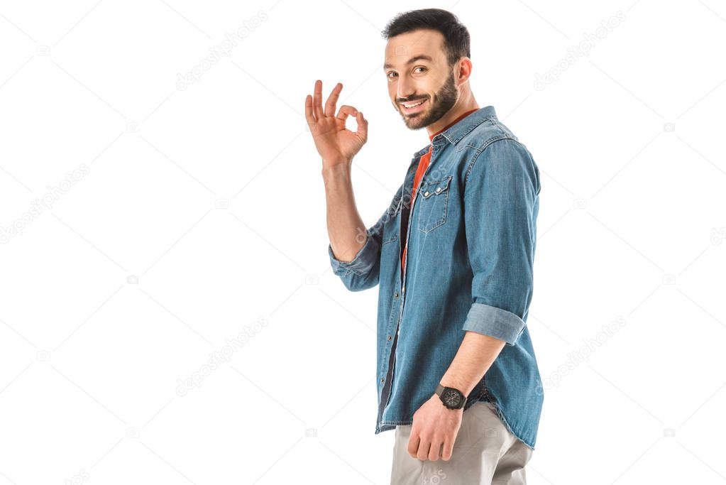 smiling man in denim shirt showing okay gesture and looking at camera isolated on white