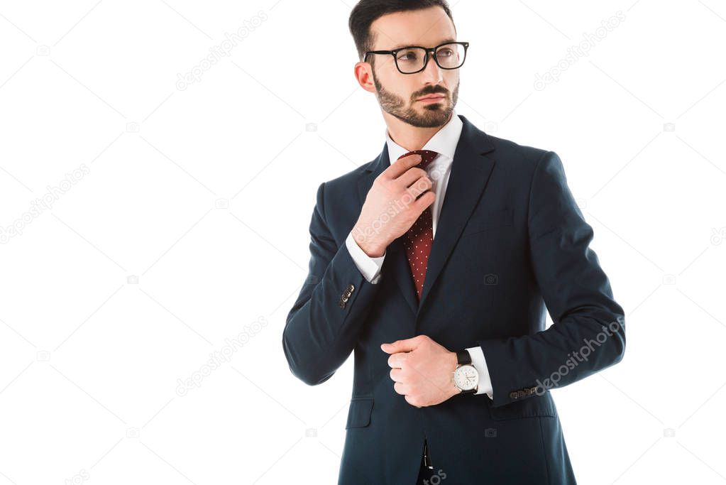 serious businessman touching tie and looking away isolated on white