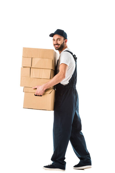 cheerful delivery man carrying cardboard boxes and looking at camera isolated on white