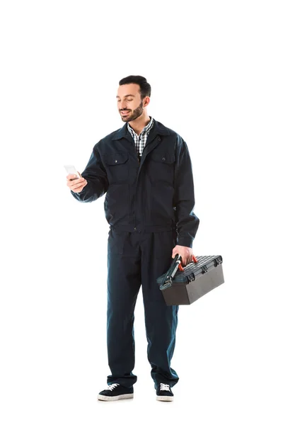 Vrolijke Workman Overalls Met Behulp Van Smartphone Holding Toolbox Geïsoleerd — Stockfoto