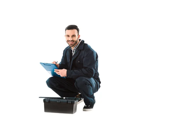 Cheerful Workman Writing Clipboard While Sitting Toolbox Looking Camera Isolated — Stock Photo, Image
