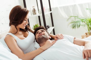 happy girlfriend looking at boyfriend lying on bed  clipart