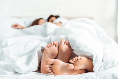 yatakta battaniye altında yatan genç kadın ve erkek yalınayak seçici odak