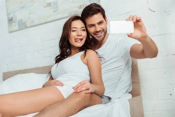 Selective Focus Happy Man Taking Selfie Girlfriend Showing Tongue Bedroom — Stock Photo, Image