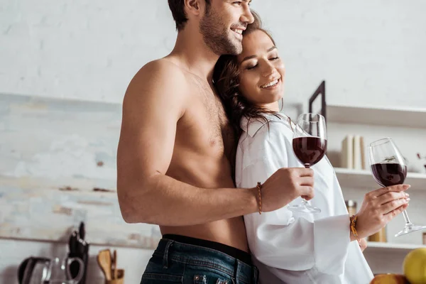 自宅で魅力的で幸せな女の子の近くにワイングラスを保持する幸せな筋肉の男の低角度ビュー — ストック写真