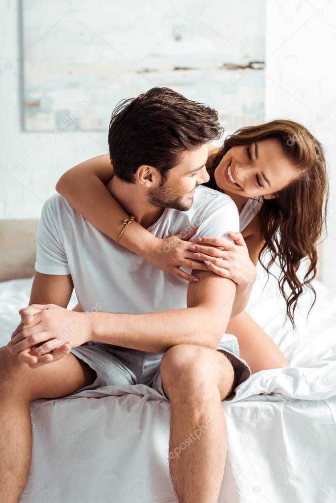 happy young woman hugging handsome boyfriend in bedroom 