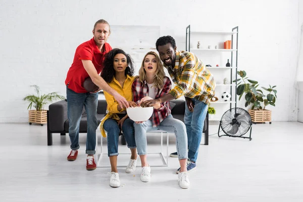 Cuatro Amigos Multiculturales Emocionados Sentados Mesa Sosteniendo Tazón Deliciosas Palomitas — Foto de Stock