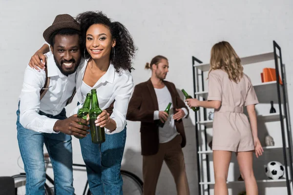 ビールのボトルを持ち 友人の近くに微笑む幸せなアフリカ系アメリカ人の男女の選択的な焦点 — ストック写真