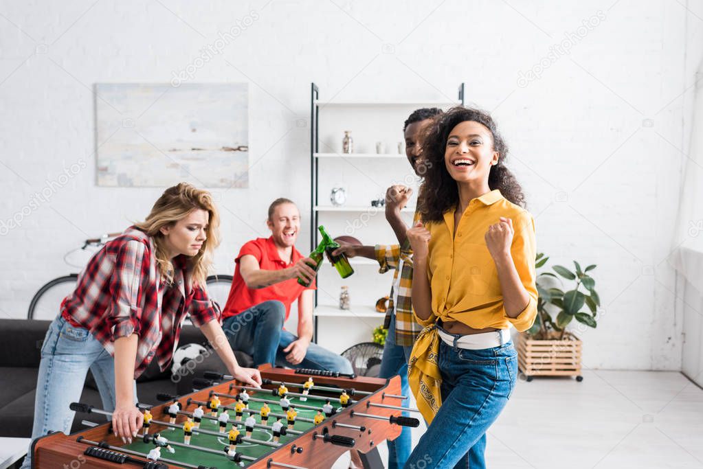 Happy and smiling multiethnic men and women playing table football in living room at home
