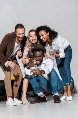 şampanya bardakları tutan arkadaşlarıile selfie çeken mutlu afrikalı-amerikalı adam düşük açı görünümü 