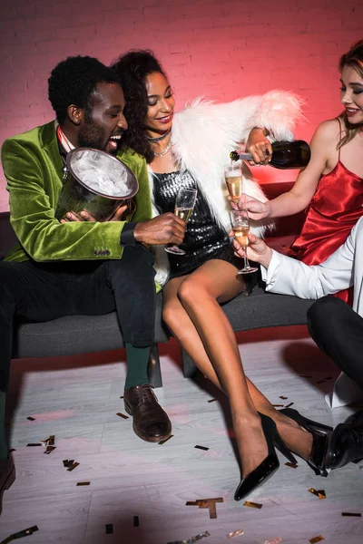 Африканская Американская Девушка Держит Бутылку Возле Бокалов Шампанского Сидя Рядом — стоковое фото