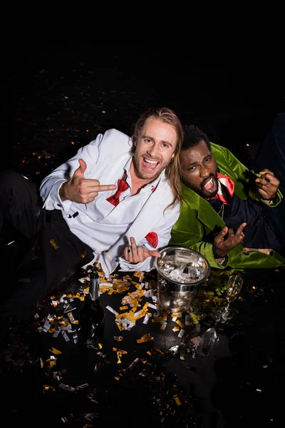 Happy Drunk Multicultural Men Showing Middle Fingers While Lying Confetti — Stock Photo, Image