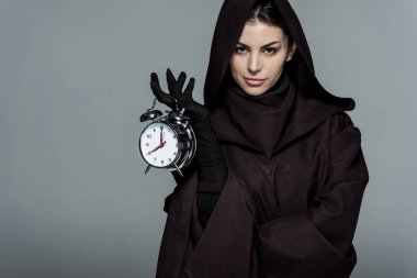 Ölüm kostümü giymiş kadın alarmlı saati gri renkte tutuyor.