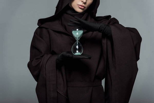 partial view of woman in death costume holding sand clock isolated on grey