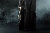 Teilansicht einer Frau im Todeskostüm mit hängender Schlinge im Rauch auf schwarz