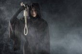 Frontansicht einer Frau im Todeskostüm mit hängender Schlinge im Rauch auf schwarz