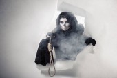 Frau im Todeskostüm hält Schlinge in der Hand und steigt aus Loch in Papier
