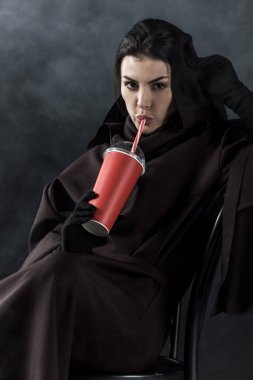 woman in death costume sitting on chair and drinking beverage on black clipart