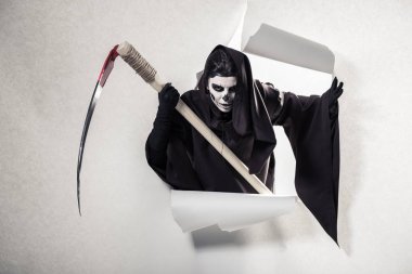 Ölüm kostümlü kadın tırpanı tutuyor ve kağıt deliğinden çıkıyor.
