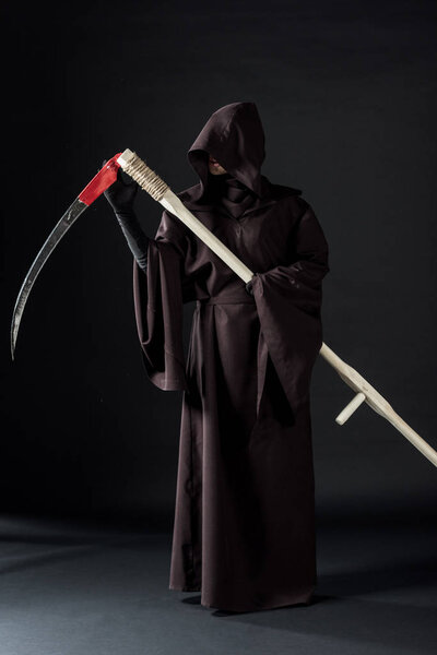 full length view of woman in death costume holding scythe on black