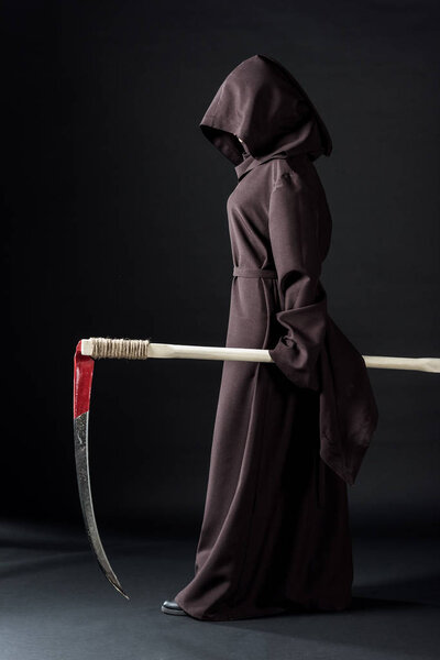 full length view of woman in death costume holding scythe on black