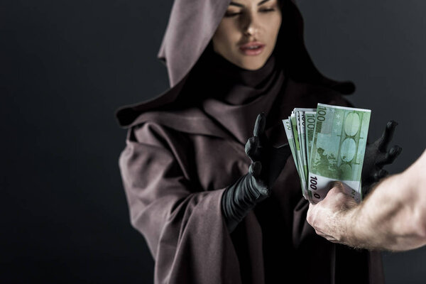 partial view of man giving euro banknotes to woman in death costume isolated on black