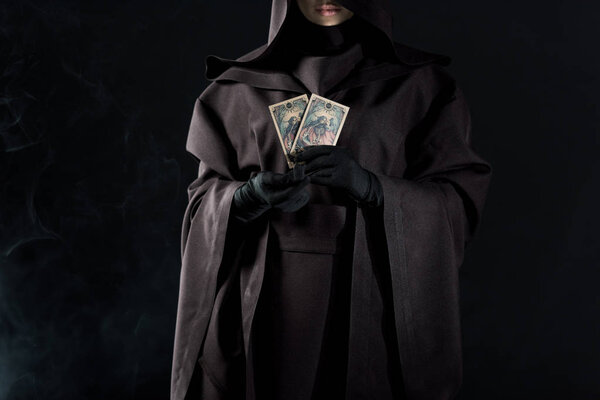 КИЕВ, УКРАИНА - 18 апреля 2019 года: обрезанный вид женщины в костюме смерти, держащей карты таро изолированные на черном
