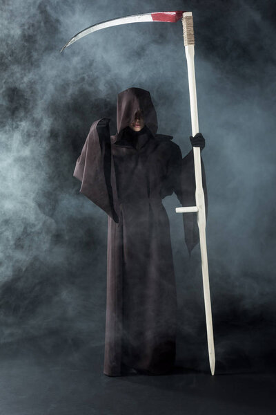 full length view of woman in death costume holding scythe on black with smoke