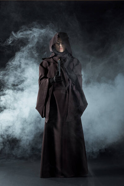 full length view of woman in death costume holding candle in smoke on black