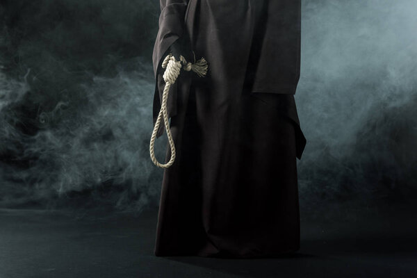 partial view of woman in death costume holding hanging noose in smoke on black