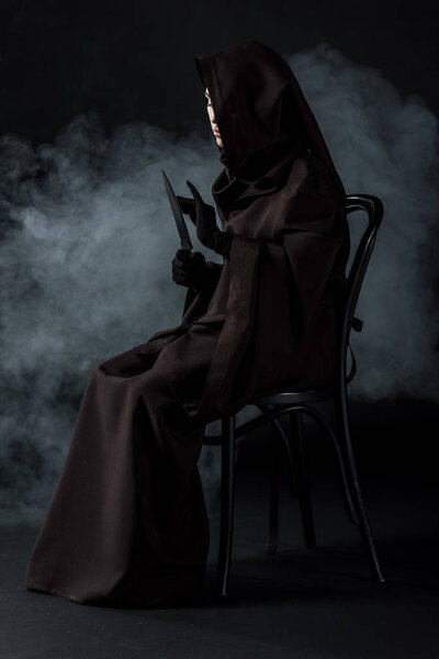 woman in death costume holding knife and sitting on chair on black