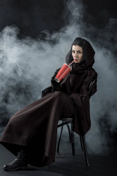 穿着死亡服装的女人坐在椅子上 喝着黑色的饮料 — 图库照片