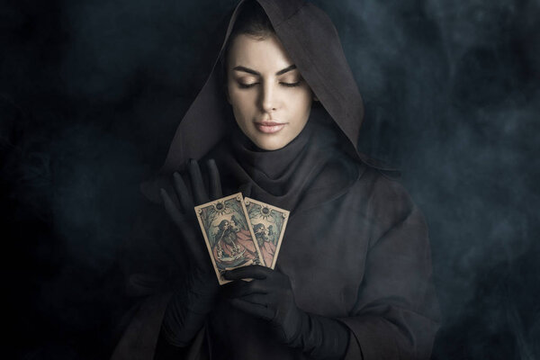 KYIV, UKRAINE - APRIL 18, 2019: attractive woman in death costume holding tarot cards on black