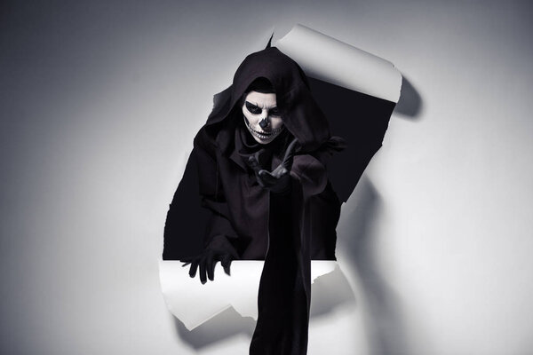woman in death costume woth outstretched hand getting out of hole in paper