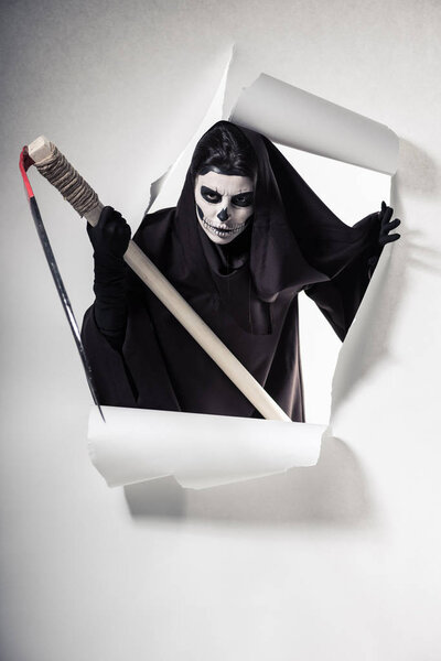 woman in death costume holding scythe and getting out of hole in paper