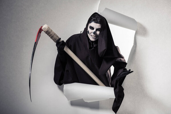 woman in death costume holding scythe and getting out of hole in paper