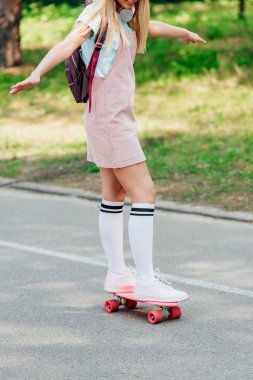 partial view of girl in knee socks skateboarding on road clipart