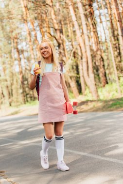 yolda portakal suyu şişesi tutan kuruş kurulu ile sarışın gülümseyen kız tam uzunlukta görünümü