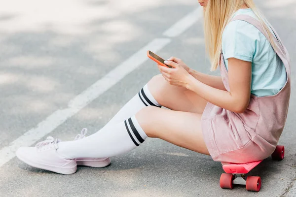 Penny Tahtası Üzerinde Oturan Yolda Akıllı Telefon Kullanarak Sarışın Kız — Stok fotoğraf