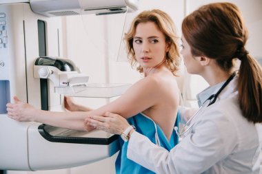 Genç radyolog, hastayı röntgen cihazında mammografi teşhisine hazırlıyor.