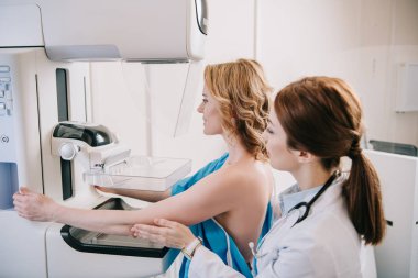 Genç radyograf, röntgen makinesinde mammografi testi yaparken hastaların yanında duruyor.
