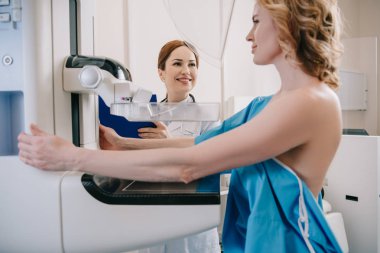 x-ray cihazında mamografi teşhisi ni yaparken hastanın yanında duran gülümseyen radyolog 