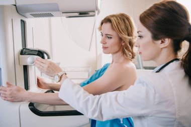 hastanın yanında dururken mamografi testi için x-ray cihazını ayarlayan özenli radyograf 
